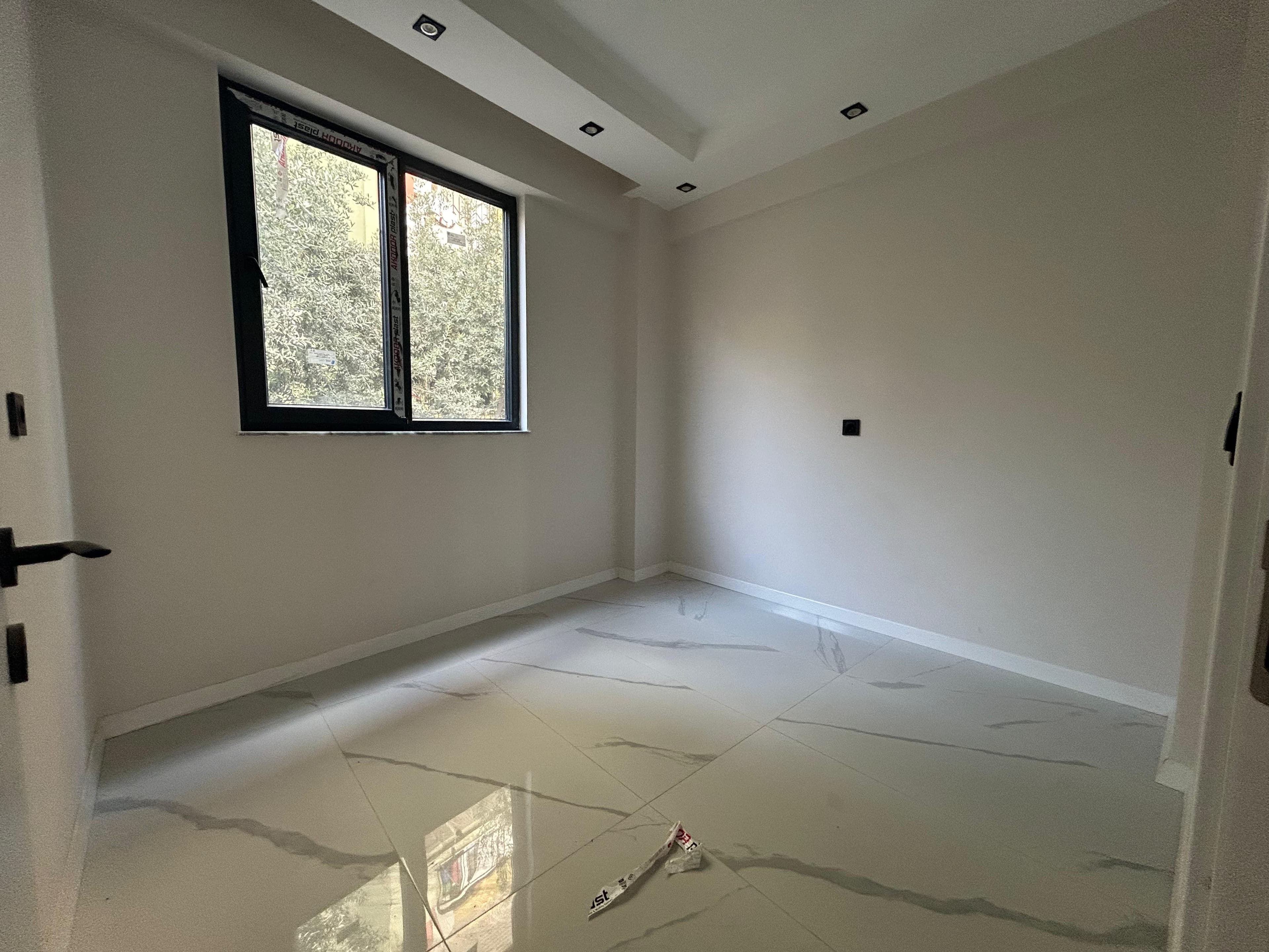 Boş oda; kademeli alçıpan tavan spot aydınlatmalı, siyah çerçeveli pencere, mermer desenli zemin, beyaz iç kapı.