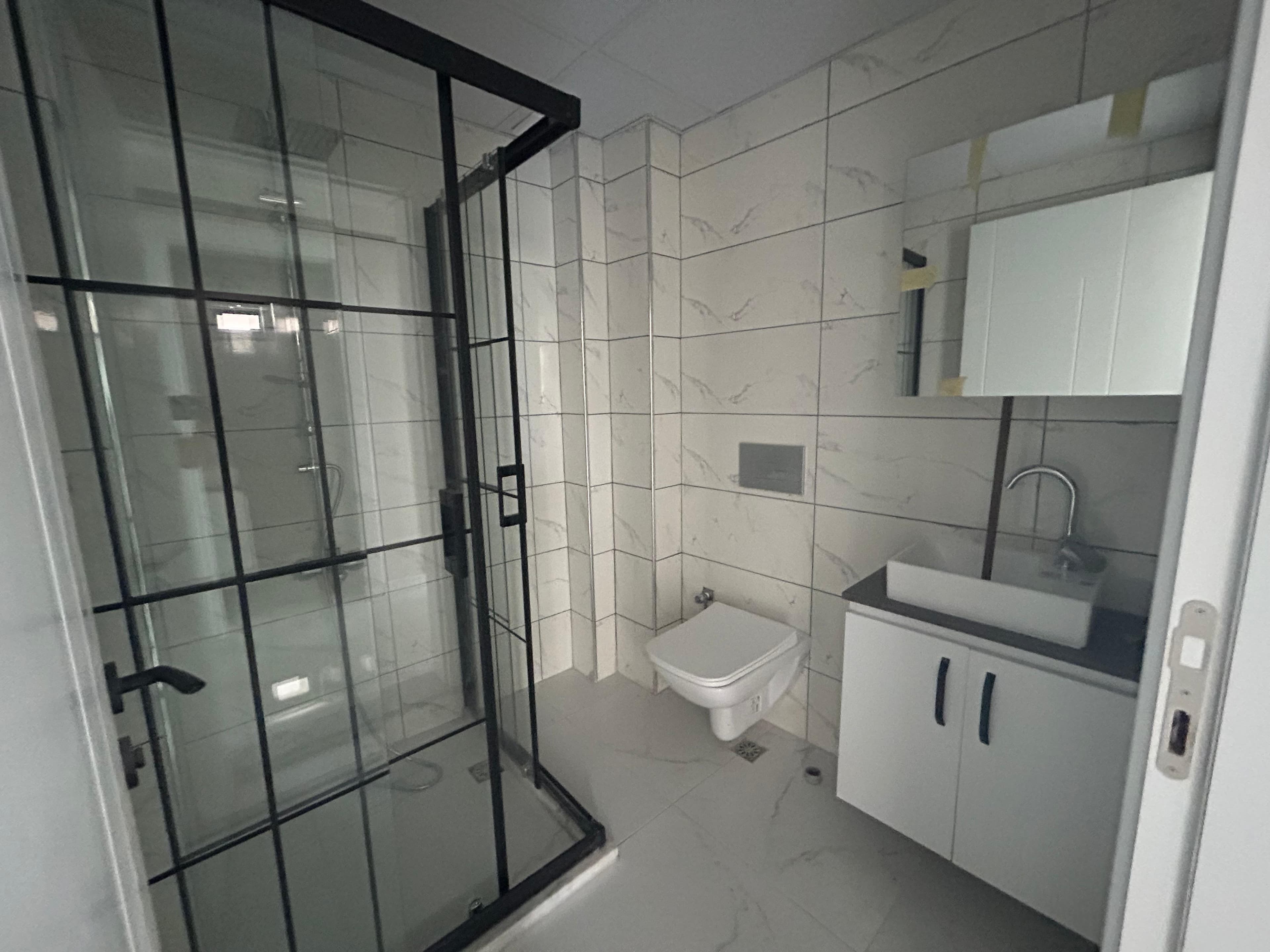 Banyo; cam duşakabin, asma klozet, lavabo dolabı, mermer desenli fayans, ayna dolabı.